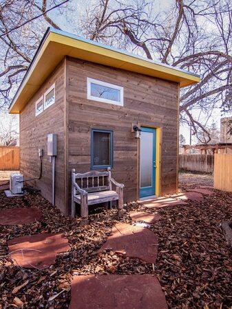 Exterior view of the tiny house, including a bench at the front and utility supply into the side of the house.