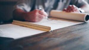 Out of focus picture of architect with long ruler and a roll of paper, from Daniel McCullough of Unsplash.
