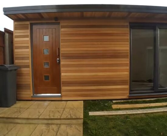 A striking, well designed backyard office workshop with timber cladding, wooden front door (into the storage area) and a corner French doors to access the main studio area.
