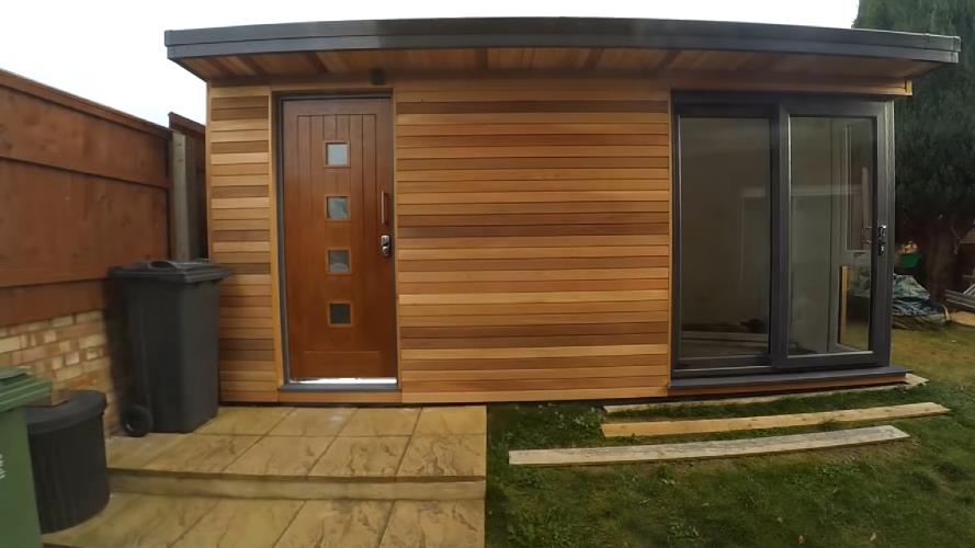 A striking, well designed backyard office workshop with timber cladding, wooden front door (into the storage area) and a corner French doors to access the main studio area.