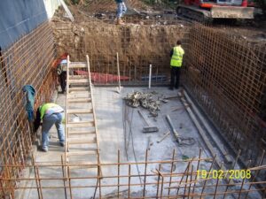 A photo showing three workmen in an approx. 10' deep hole with concrete floor and steel rebar in the walls (getting ready for the wall construction/pour).