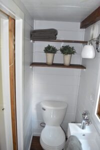 Bathroom photo showing toilet and sink, along with shelves on the wall for extra storage.