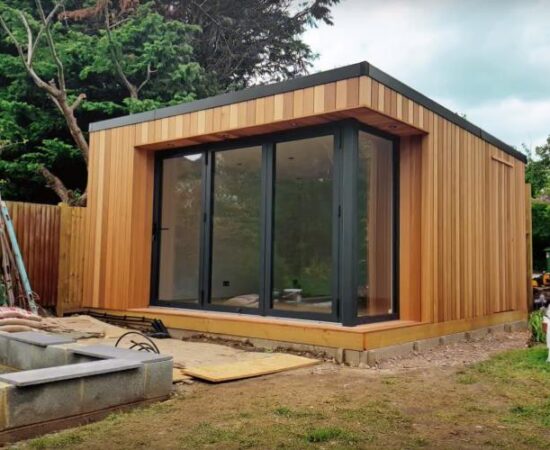 Outside photo of a UK based garden studio, with vertical wood cladding and black UPVC features.