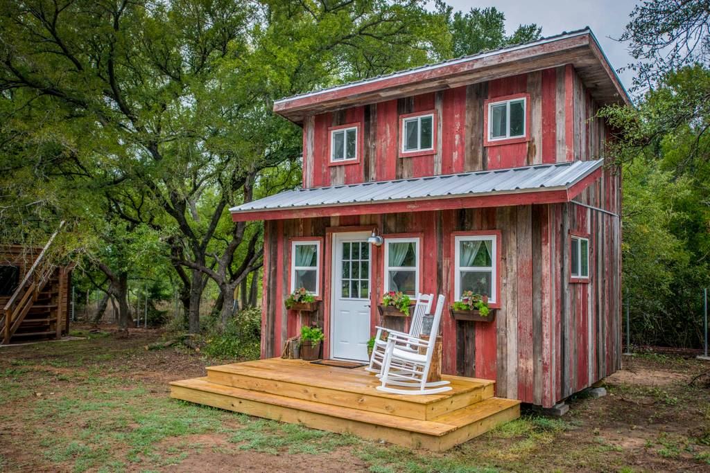 Outside of the Little Red Hen Cabin in Texas, showing a two-story tiny house and two-tier height wood front porch.