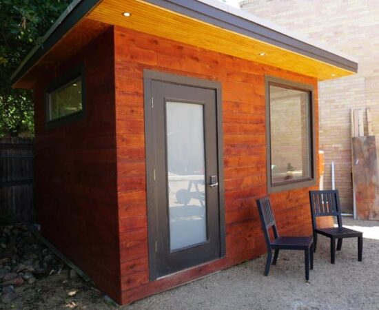 Exterior photo of Mr Money Mustache's 'tiny home', a backyard office with dark red siding and downlights in the soffit.