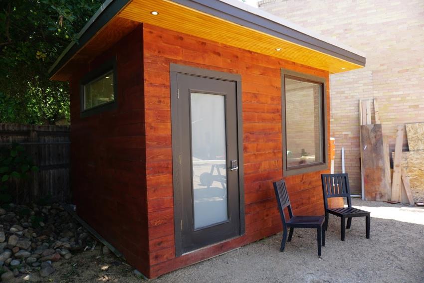 Exterior photo of Mr Money Mustache's 'tiny home', a backyard office with dark red siding and downlights in the soffit.