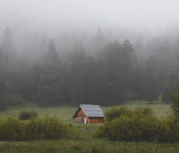 An off-grid rang in Oregon with solar panels on the roof, with foggy trees in the background. Photo from Alex Bierwagen of Unspalsh.