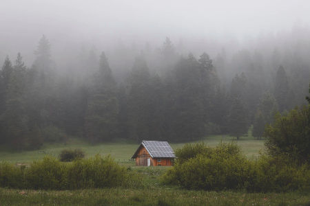 An off-grid rang in Oregon with solar panels on the roof, with foggy trees in the background. Photo from Alex Bierwagen of Unspalsh.