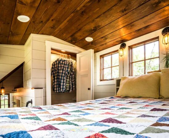 Timbercraft Tiny Homes' Denali gooseneck tiny house; a look at the master bedroom with a double bed and in-built storage via a wardrobe.