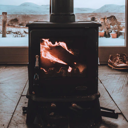 A black wood/log burning stove in the middle of a room, with mountains in the background (seen through the glass doors), from Michael Shannon of Unsplash.