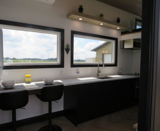 window withs modern kitchen hudson tiny home, with two seated areas.