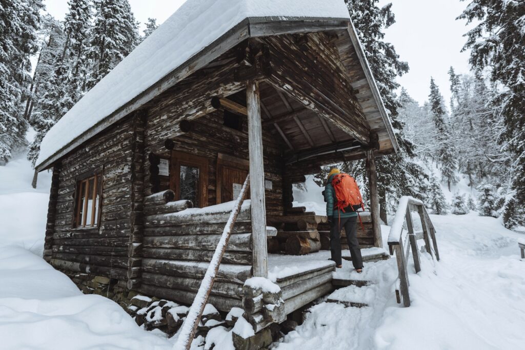 Wood-cabin-in-the-mountains-with-a-backpacker-walking-in